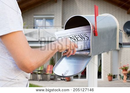Close-up Of Hand Taking Newspaper From Mailbox In Front Of Their House