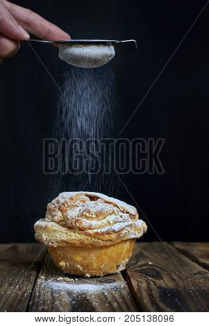 Hand sprinkling powdered sugar on a Mirliton cupcake traditional sweet of France and Basque Country Spain.