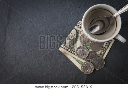 Top view of an empty coffe cup with a one dollar bill and some quarter dollars