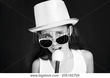 Little girl rocker with sunglasses microphone and hat on a black background