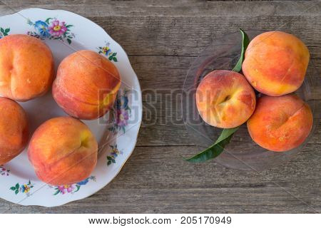 Three ripe peaches with green leaves in a plastic plate and peaches on the ceramic plate on the old wooden background