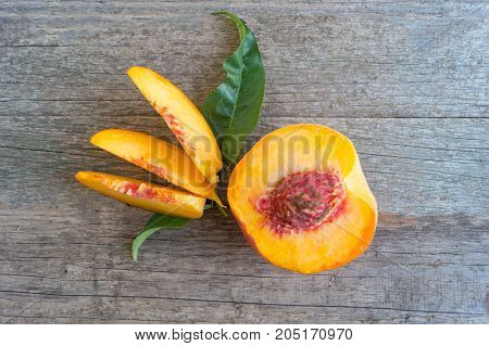 One ripe peache with slices and green leaf on the wooden background