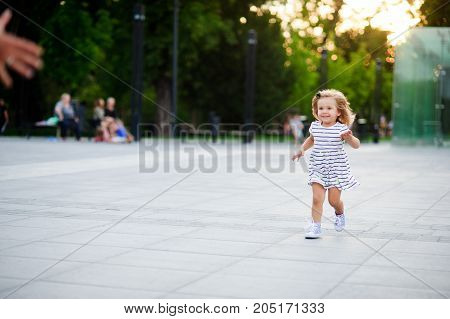 Adorable little girl runs towards the parent hands. Warm summer day. Baby is very fun.