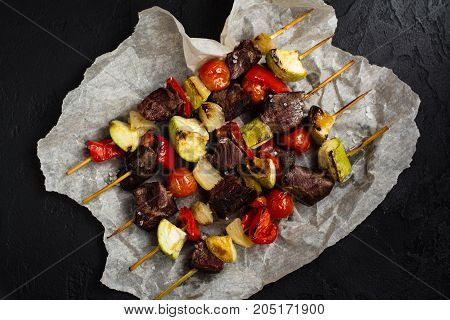 Grilled meat and vegetables cabobs with tomato sauce and sea salt over black stone table. Top view