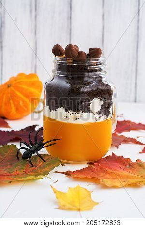Layered halloween dessert with pumpkin jello, cream and chocolate cookies in glass jars on autumn background. Selective foucs