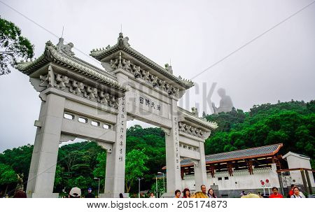 HONG KONG - MAY 31: Tourists at the gate to Po Lin Monastery with Tian Tan Buddha statue up on the hill in background, Ngong Ping Village, Lantau Island, Hong Kong