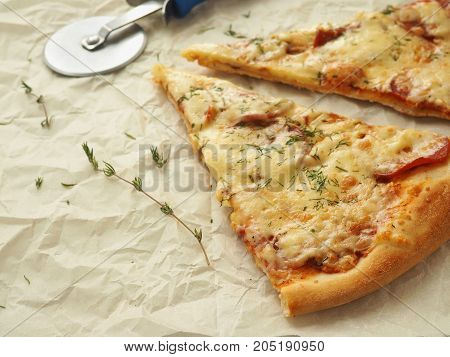 Culinary background with two pieces of  pepperoni pizza upon baking parchment. Homemade pizza with thyme. Copy space for your text. Selective focus.