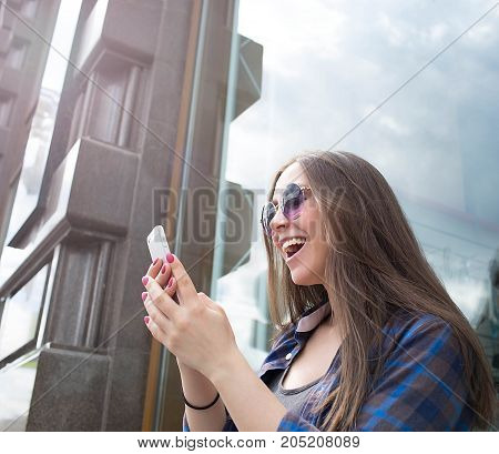 Young happy woman received good news in text message on mobile phone. Smiling hipster girl using cell telephone for talk with friends via internet