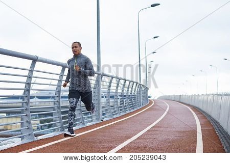 Healthy active lifestyle concept. Attractive young African male jogger exercising at stadium alone early in the morning. Muscular dark-skinned sportsman in trendy outfit getting ready for marathon