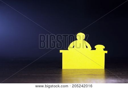 Paper man bureaucrat sitting on table against dark background