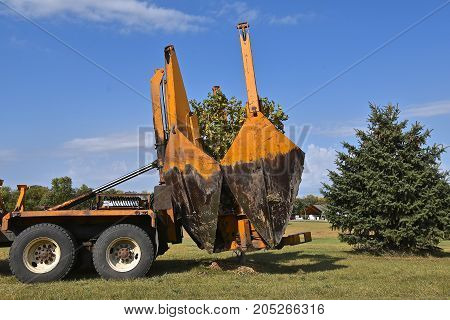 The mounted spade, jaws, and bucket are part of a tree removal  and transplanting machine and is lifting the jaws after dropping the tree into a hole