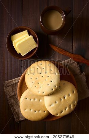 Traditional Chilean Hallulla bread rolls on wooden plate with butter and coffee with milk above photographed overhead on dark wood with natural light