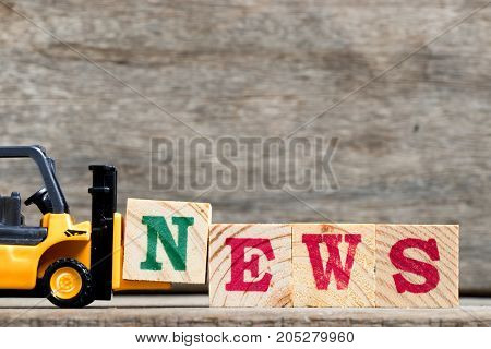 Yellow plastic forklift hold letter N to complete word news on wood background