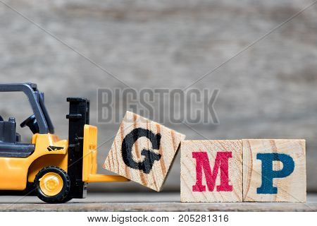 Yellow plastic forklift hold letter G to complete word GMP (Abbreviation of Good Manufacturinc Practice) on wood background