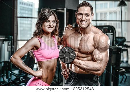 Handsome young muscular Caucasian man and woman working out training in the gym gaining weight pumping up muscles and poses fitness and bodybuilding concept