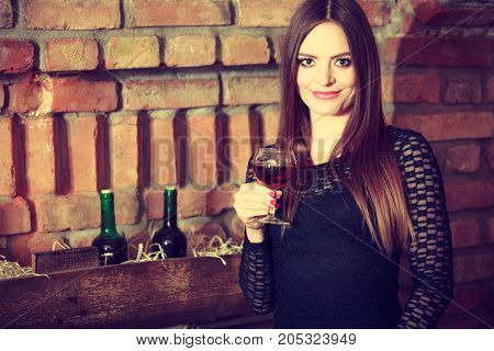 Elegant beauty lady long hair full make up wearing black dress tasting wine in rural cottage interior celler