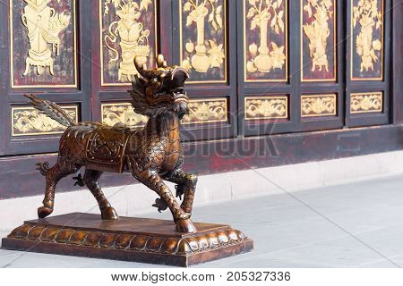 Bronze dradon statue in a buddhist monastery with a decorated wall in the background, Chengdu, China