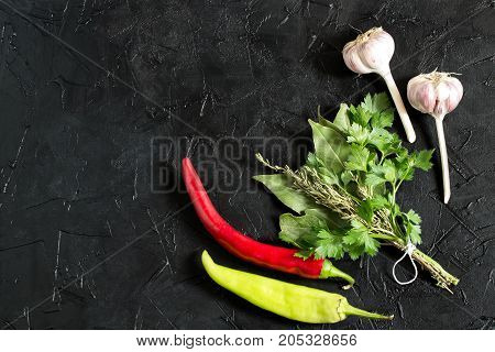 Bouquet garni and spicy vegetables. Bay leaf parsley and thyme bound with culinary thread chili pepper and garlic on black textured background