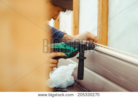 A worker installs panels beige siding on the facade of the house
