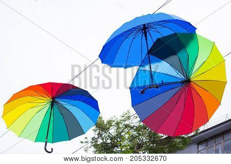 Bright umbrellas in festive decoration of city. Hanging multicolored umbrellas in sky above street. Avenue of flying umbrellas. Mood of joy and happiness