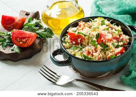 Bowl with couscous vegetables and herbs on pale gray background with green gauze napkin. Traditional food in cuisine of Maghreb. Vegetable ingredients: tomatoes and parsley. Dietary and healthy food