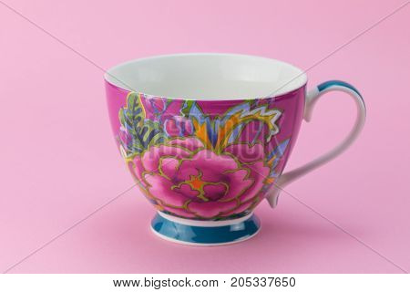 Side view of empty tea or coffee cup with pink and purple flower decoration isolated on pink background