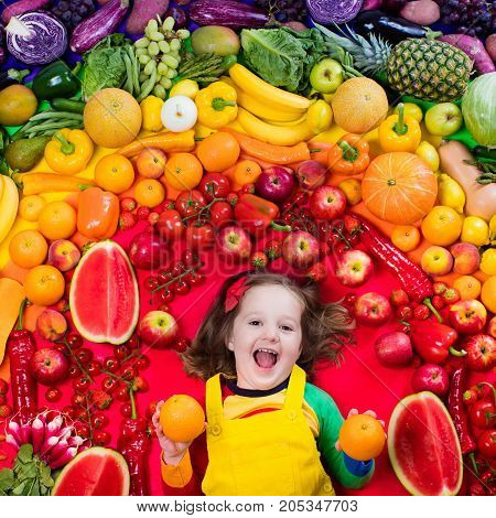 Little girl with variety of fruit and vegetable. Colorful rainbow of raw fresh fruits and vegetables. Child eating healthy snack. Vegetarian nutrition for kids. Vitamins for children. View from above.