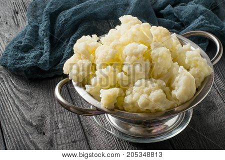Blanched cauliflower in colander on gray wooden background. White cauliflower inflorescences in metal colander gray gauze napkin on table. Preparing for diet dinner