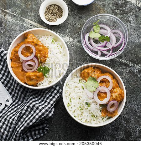 Homemade dinner butter chicken on cream with spices, cream served with basmati rice in ceramic bowls with cilantro and sweet red onion. Top View