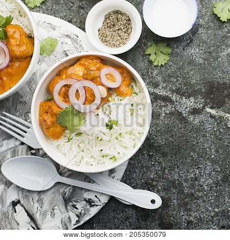 Homemade dinner butter chicken on cream with spices, cream served with basmati rice in ceramic bowls with cilantro and sweet red onion. Top View