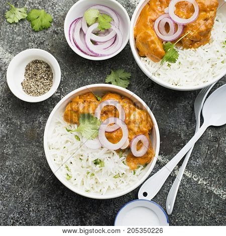 Homemade dinner butter chicken on cream with spices, cream served with basmati rice in ceramic bowls with cilantro and sweet red onion. Top View