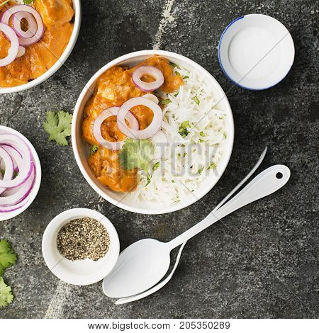Homemade dinner butter chicken on cream with spices, cream served with basmati rice in ceramic bowls with cilantro and sweet red onion. Top View