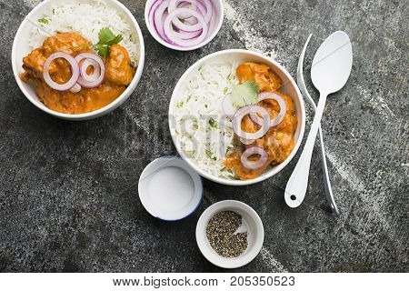 Homemade dinner butter chicken on cream with spices, cream served with basmati rice in ceramic bowls with cilantro and sweet red onion. Top View