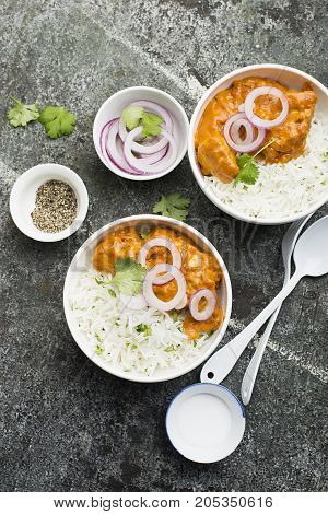 Homemade dinner butter chicken on cream with spices, cream served with basmati rice in ceramic bowls with cilantro and sweet red onion. Top View