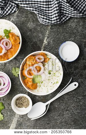 Homemade dinner butter chicken on cream with spices, cream served with basmati rice in ceramic bowls with cilantro and sweet red onion. Top View