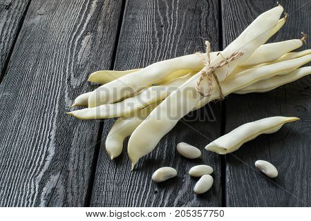 Bunch of white string beans tied with twine. Long white pods and seed beans on dark wooden table. New harvest. Ingredient in healthy and dietary food