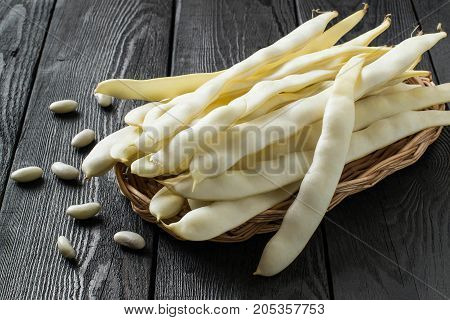 White string beans on wicker tray. Long white pods and seed beans on dark wooden table. New harvest. Ingredient in healthy and dietary food