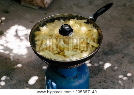 Fried potatoes in a frying pan in the yard on a gas burner
