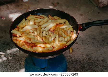 Fried potatoes in a frying pan in the yard on a gas burner