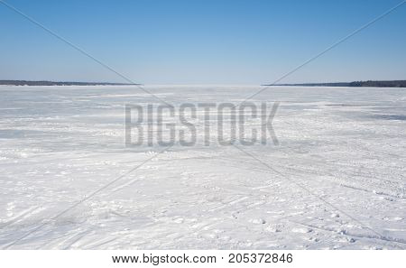 Bay covered in ice with footprints and tracks under clear blue sky against shore on both sides on Lake Simcoe Ontario Canada.