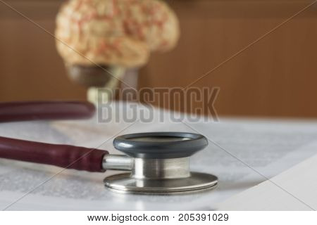 A red stethoscope on the texbook with brain model on background.