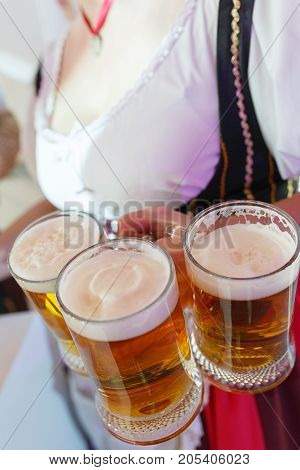 Girl in a traditional dress with a big breasts and deep neckline holds full mugs of beer during the celebration of the Oktoberfest