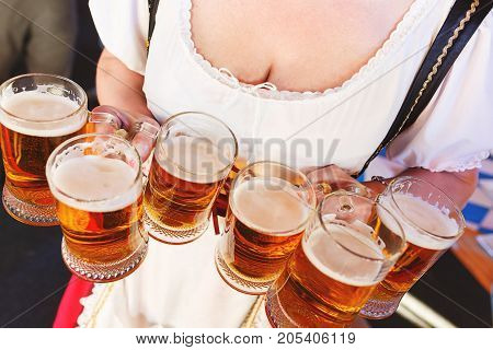 Girl in a traditional dress with a big breasts and deep neckline holds full mugs of beer during the celebration of the Oktoberfest