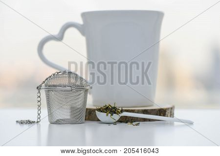Dry tea leaves in a teaspoon with Tea strainer and cup