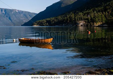 Peaceful scenery with orange wood fishing boat in the river. Norway landscape with mountains in Lustrafjord