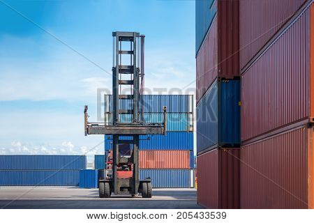 Forklift truck lifting cargo container in shipping yard or dock yard against sunrise sky with cargo container stack in background for transportation import,export and logistic industrial concept