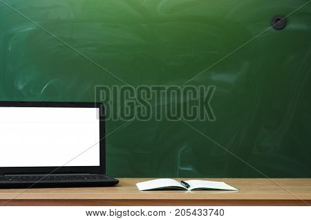 Teacher or student desk table on school blackboard background. Education background. Mockup education concept. Laptop with blank screen and copy book on the table.