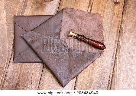 handmade, hobby, business concept. on the dark wooden table there are few unusual envelopes created of dark brown natural leather and excellent stamp with elegant handle