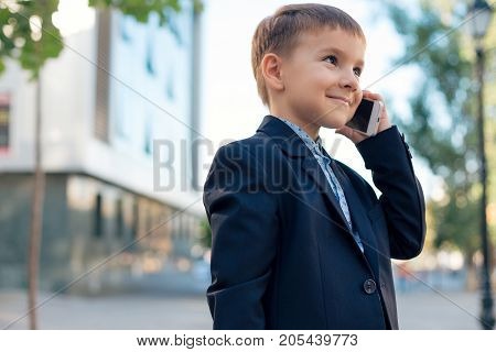 Concept future businessman. Business meeting. Low angle of future businessman in dark blue jacket holding white phone to ear listening to somebody, urban background.