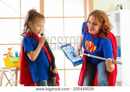 Happy woman and kid daughter is preparing for room cleaning. Mother and her child girl playing together. Family in Superhero costumes.